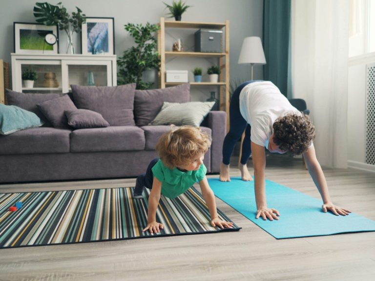 Mutter macht Yoga neben einem spielenden Kind im Wohnzimmer.